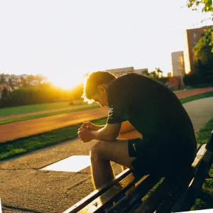 photo of a boy sitting on a bench with head down - seems thoughtful