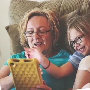 photo of woman and child on sofa laughing while using a tablet device