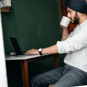 Indian Man wearing turban on laptop drinking a coffee