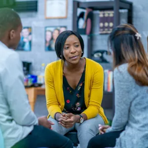 photo of black woman sitting with two students.  she is listening to them
